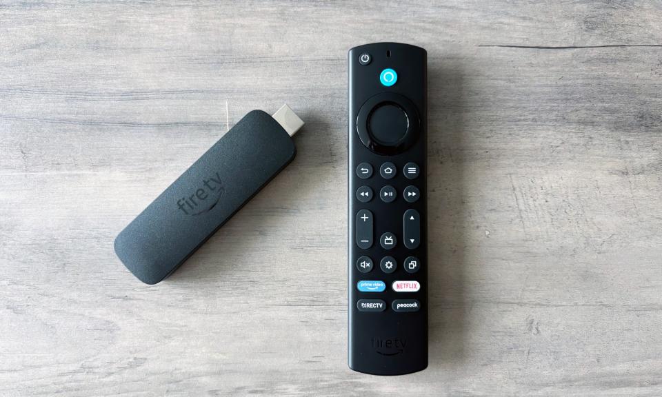 The Amazon Fire TV Stick 4K Max rests on a brown wooden tabletop next to its included remote.