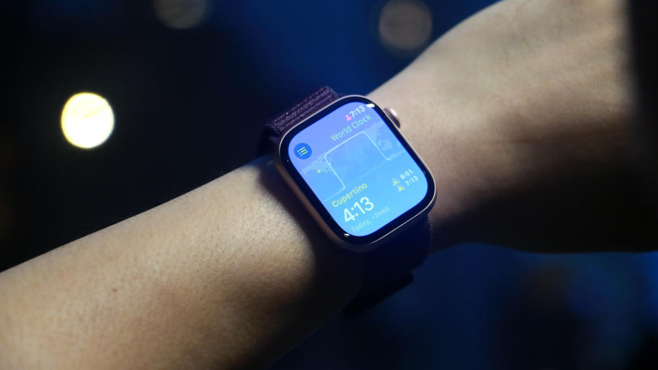 A person wears the Apple Watch Series 10 on their wrist. It shows a blue screen with the time and other widgets. 