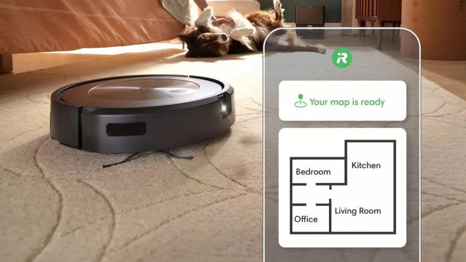 A robot vacuum on  a rug with a dog on its belly in the background. Overlaid is a smartphone outline, showing the home map.