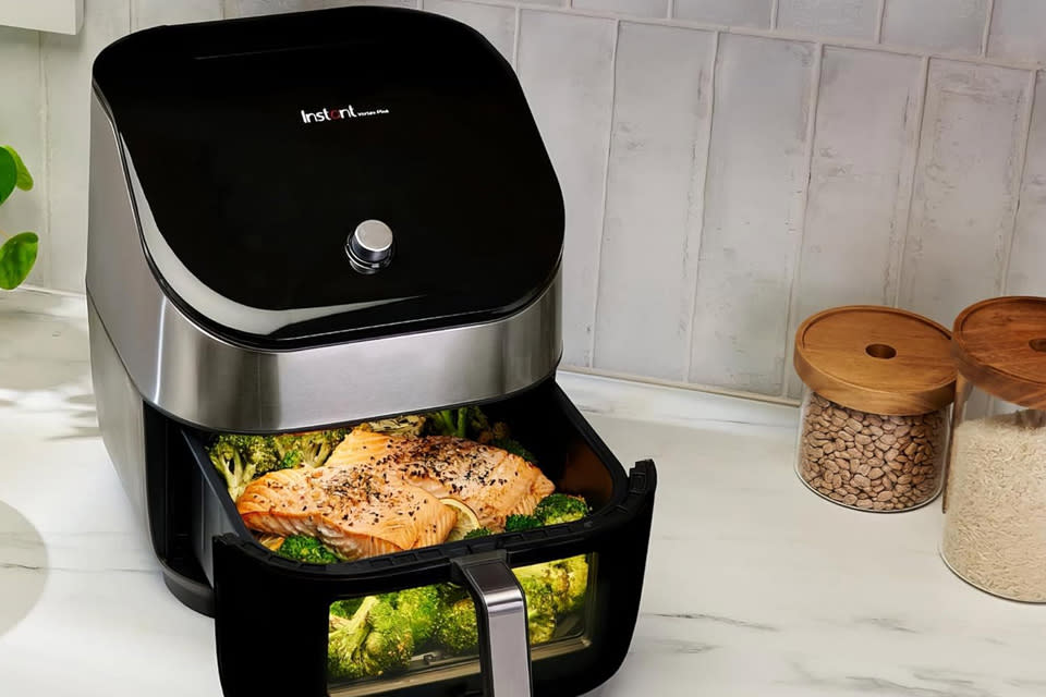 The Instant Vortex Plus air fryer sits on a countertop with some retro rice and beans jars in the background. 