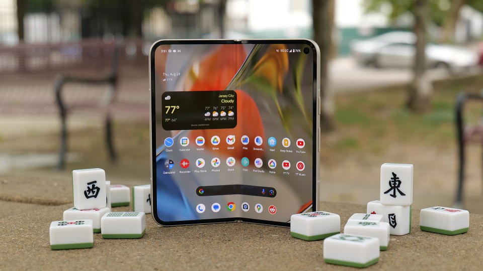 The Pixel 9 Pro Fold slightly folded, with its internal display facing out. It's sitting on a park table with mahjong tiles scattered around it.